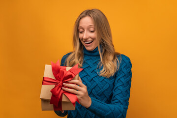 Charming young woman open a gift with red ribbon. Studio shot, yellow background. New Year, Birthday, Holiday concept