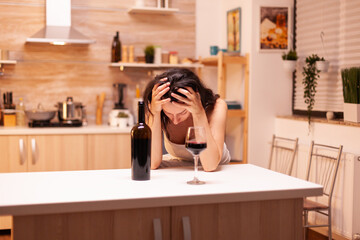 Woman with alcoholic beverage is drinking alone a bottle of wine that get her hangover. Unhappy person disease and anxiety feeling exhausted with having alcoholism problems.