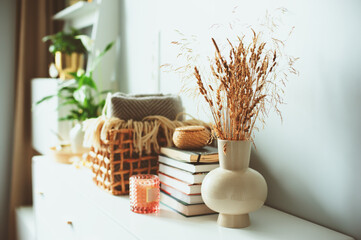 cozy modern interior details with fluffy reeds, candles and books in beige tones. Minimalist nordic...