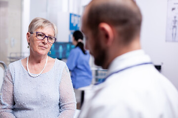 Fototapeta premium Woman listening doctor during examination in consultation clinic room. Converstation with medical stuff clinic medicine healthcare, senior, coat, clipboard.