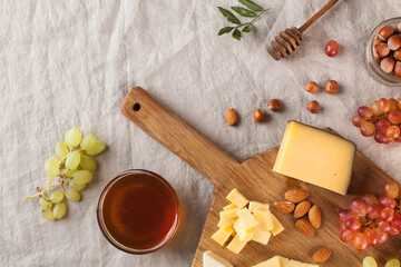 Cheese plate. Assorted cheeses on a wooden Board with grapes, honey, nuts on a linen tablecloth. Copy space.
