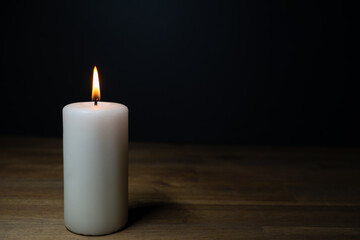 Fototapeta na wymiar A white burning candle on a wooden table, dark background and copy space