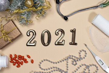 New Year's card on medical subjects: figures 2021, phonendoscope, tablets, thermometer and bandage with spruce branch on a beige background. New Year 2021 medicine.