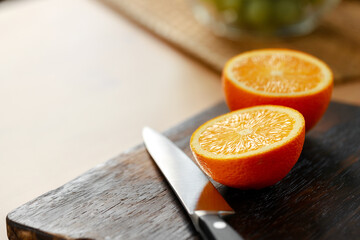 Cut orange and knife on wooden cutting board on table