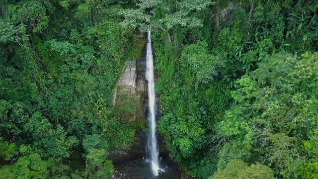 Aerial view of a majestic tall waterfall inside the jungle. People inside the water 4K