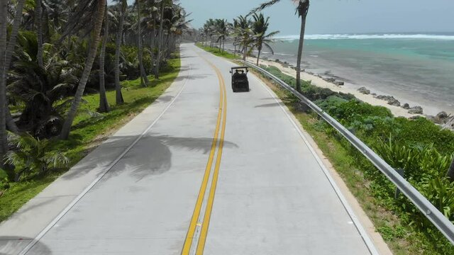 Drone following a golf car on a road next to the beach of the Caribbean Sea in San Andres, Colombia 4K