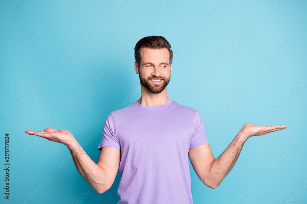 Poster Photo of young handsome guy hold palms balance promo demonstrate product look empty space isolated over blue color background