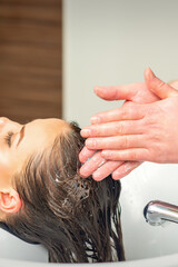 Fototapeta premium Beautiful young woman washing her hair by hands of male hairdresser in hair salon