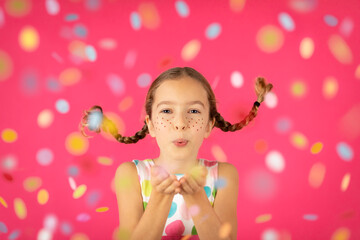 Obraz na płótnie Canvas Fancy child with pigtails blowing confetti against pink background