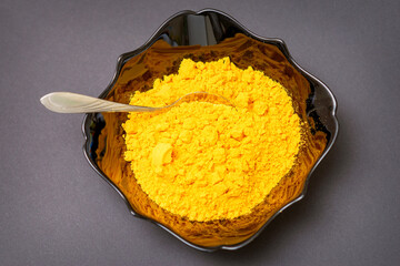 Top view closeup of turmeric or curcuma powder in ceramic black bowl or deep plate on dark background. Flat lay