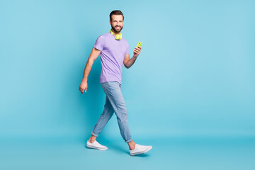 Fototapeta na wymiar Full length body size photo of hipster wearing casual clothes headphones keeping smartphone isolated on bright blue color background