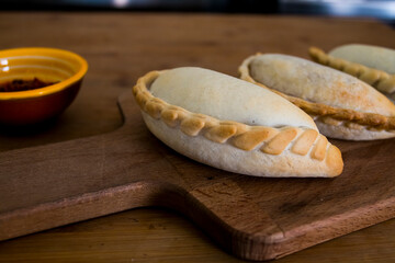 Traditional baked Argentine empanadas savory pastries with meat beef stuffing or vegetables against wooden background and spicy sauce. Latin American fried food