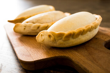 Traditional baked Argentine empanadas savory pastries with meat beef stuffing or vegetables against wooden background and spicy sauce. Latin American fried food
