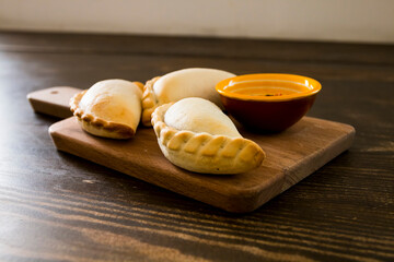 Traditional baked Argentine empanadas savory pastries with meat beef stuffing or vegetables against wooden background and spicy sauce. Latin American fried food