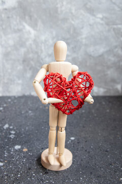 Wooden mannequin with red rattan heart. On grey background