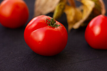 red ripe tomatoes and autumn dried leaves lie on a black background . High quality photo
