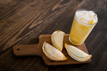 Traditional baked Argentine empanadas savory pastries with meat beef stuffing and vegetables against wooden background with spicy sauce and ice lemon tea, fresh and homemade. Latin food and drink