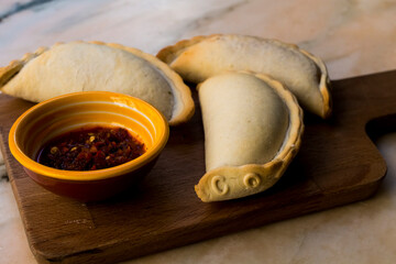 Traditional baked Argentine empanadas savory pastries with meat beef stuffing or vegetables against wooden background and spicy sauce. Latin American fried food