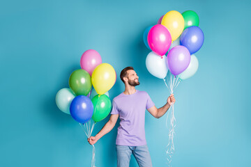 Photo portrait of guy holding helium balloons in two hands isolated on pastel blue colored background