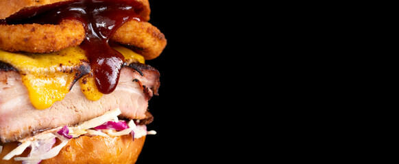 Juicy burger with bbq pork rib, onion rings, cheese, cabbage and sauce isolated on black. Copy space