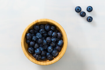 Full wooden bowl of blueberries with white background. Purple fresh berries in woody dish on table with copy space. Heap of raw healthy sweet fruit with space for text.