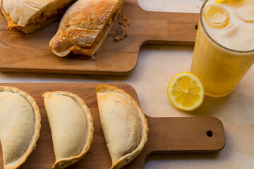 Traditional baked Argentine empanadas savory pastries with meat and a sandwich beef stuffing with tasty bread against wooden background. Healthy food served with a ice lemon tea, fresh and homemade