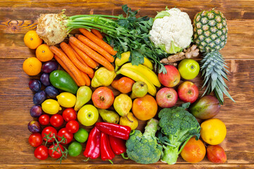 Fresh raw fruit and vegetable on brown wooden table. Many sorts of healthy vegan food from garden on brown desk. Group of colorful plants lying flat from above.