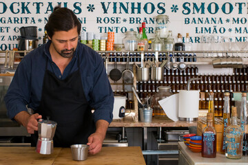Male Barista preparing fresh espresso in coffee maker for customer in a fancy coffee shop. Cafe owner serving a client at the coffee shop