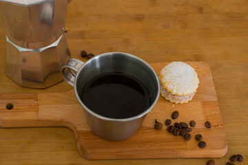 Italian lack coffee in a cup with coffee beans and a handmade cookie with sugar and a moka pot behind. Everything in vintage brown background close to the window.