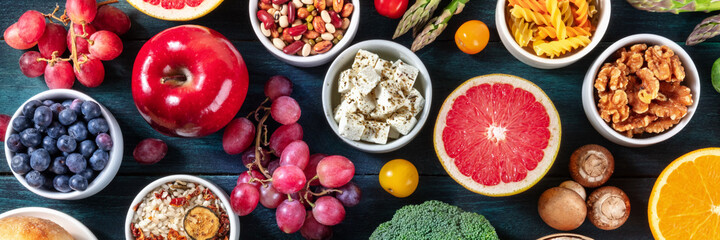 Vegetarian food panorama with fruit and vegetable, cheese, nuts, legumes and other products, overhead flat lay shot on a dark wooden background