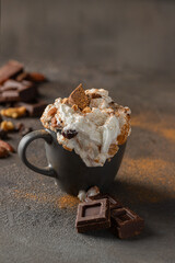 Hot chocolate cocoa cup with whipped cream decorated with cinnamon, chocolate slice and nuts  on concrete background. Traditional beverage for cold days concept.