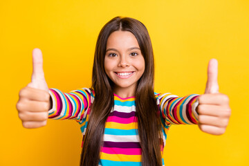 Photo of small girl raise two thumbs up beaming white smile look camera wear striped shirt isolated...