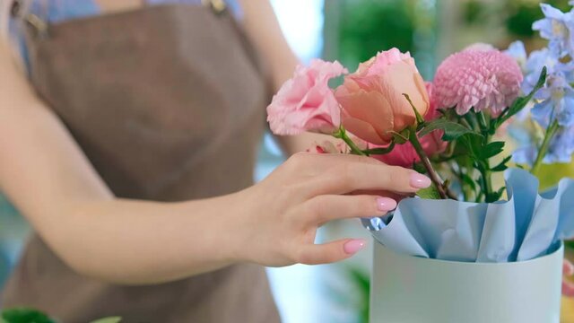 florist hands prepare tender bouquet with blooming flowers in light blue hat box close view slow motion