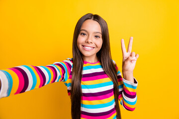 Photo of little adorable girl take selfie show v-sign beaming smile wear striped shirt isolated yellow color background