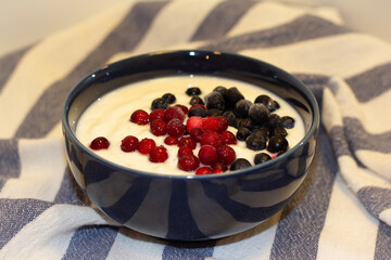 A bowl of yoghurt sprinkled with lingonberries and blueberries on a tablecloth.