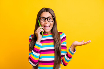 Photo portrait of amazed girl talking on mobile phone laughing wearing striped jumper isolated on vibrant yellow color background