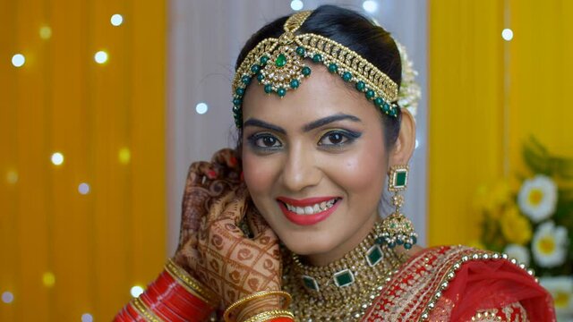 Young Indian bride smiling - Putting on beautiful earrings for her wedding function . Closeup shot of a Punjabi bride with Mehendi/Henna decorated hands getting ready for her matrimonial day - Indi...