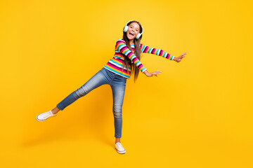 Full length body size photo of laughing girl with headphones smiling dancing balancing isolated on bright yellow color background