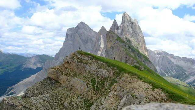 Beautiful clouds above and fantastic Seceda mountains below with  people hiking in the distance. at the fantastic Seceda mountain hiking trail, shot in 4K resolution. Seceda Summit, Italy.