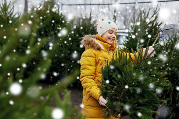 winter holidays and people concept - happy smiling little girl choosing christmas tree at street...