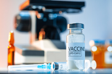 Vial of Covid-19 vaccine next to a microscope