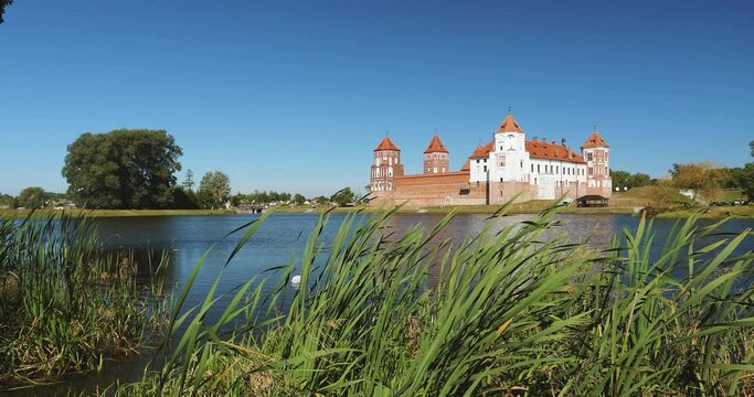Mir, Belarus. Mir Castle Complex From Side Of Lake. Architectural Ensemble Of Feudalism, Ancient Cultural Monument, UNESCO World Heritage Site. Famous Landmark In Summer Sunny Day Under Blue Sky, Set.