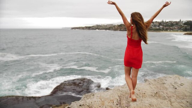 Girl Put Hands In The Air As She Watches The Crashing Waves In The Rocks - Eastern Suburbs, Sydney, New South Wales, Australia. - wide shot