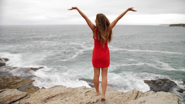 Girl Raising Both Hands In The Sky While Enjoying The Ocean Waves Crashing On The Rocks - Eastern Suburbs Beach - Sydney, NSW, Australia. - wide shot