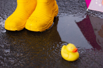 Rubber yellow boots stand in a puddle next to lies a yellow rubber duckling. bad weather