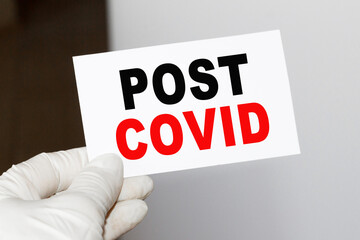 The doctor's hands show the word POST COVID - . a gloved hand on a white background. Medical concept. the medicine