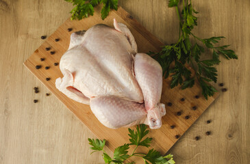 Whole raw chicken on the cutting board, with green parsley and allspice, ready to cook.