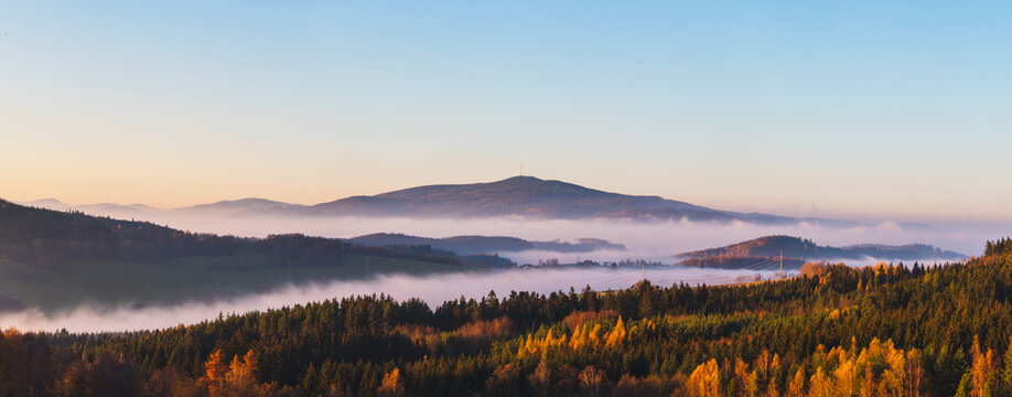 misty landscape at sunset, mountains rising from clouds of fog in the background, clear sky - mountain Klet, Czech republic