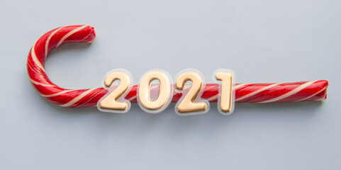 Golden new year numbers 2021 glued to a sweet candy stick of Santa Claus on a blue background, top view, flat lying