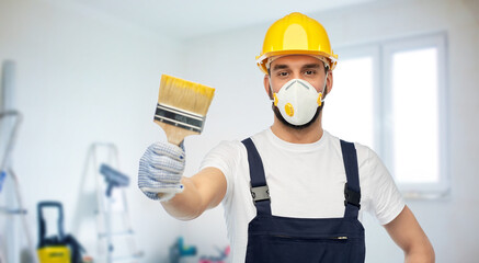 Fototapeta na wymiar repair, construction and building concept - male worker or builder in yellow helmet and respirator with brush over room with equipment on background